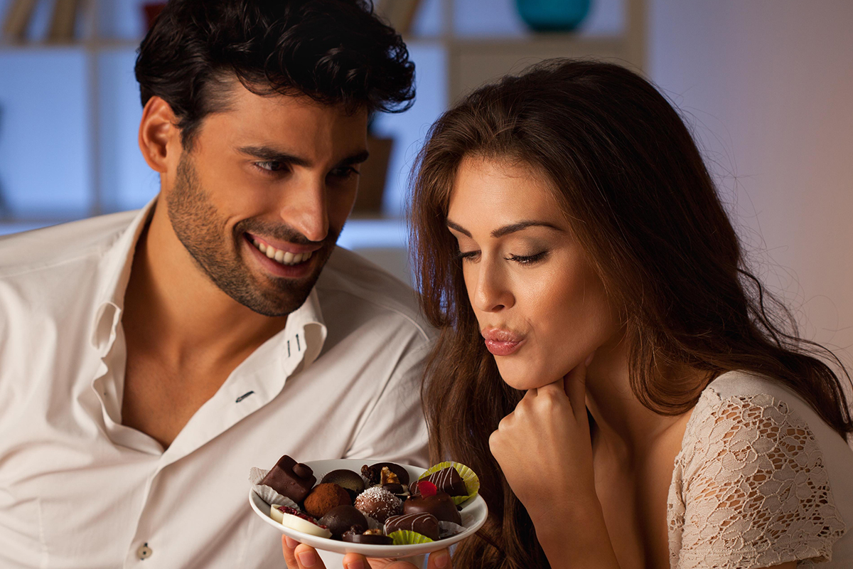 Romantic couple having dinner at home. Man offering chocolate to woman.